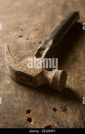 vintage rusty iron claw hammer with worn dark handle on wood workbench surface, close-up soft focus with copy space Stock Photo