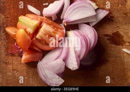 fresh chopped red tomatoes and sliced raw onions on wooden cutting board surface, top view close-up with copy space Stock Photo