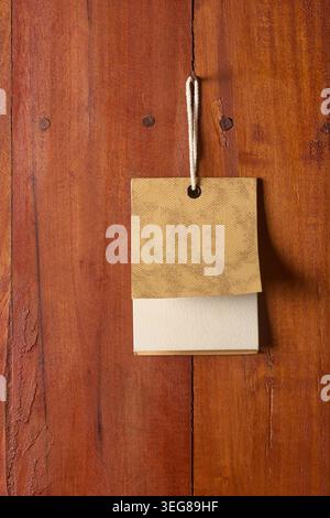 blank rectangular paper hang tag on brown wood plank surface, white cord hanging from nail, copy space of retail price tag mockup template Stock Photo