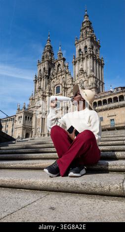 African woman in a sweatsuit and hat drinking from a reusable bottle on the Santiago Cathedral steps. Stock Photo