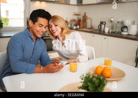 Happy couple laughing watching content on smartphone in kitchen Stock Photo