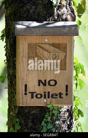 Wooden 'No Toilet' sign with image of video camera mounted on tree in forest warning visitors to respect nature, Obertraun, Lake Hallstatt, Austria Stock Photo