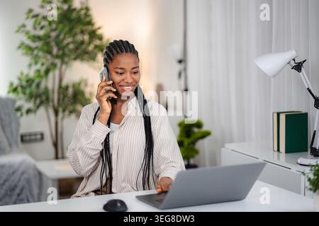 Black woman smiling, talking on phone, working from home Stock Photo