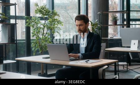 Concentrated Caucasian businessman typing laptop in modern office writing notes professional male entrepreneur corporate employer manager researching Stock Photo