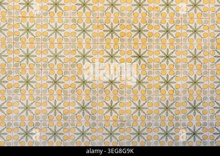 Repeating floral tile pattern features yellow circular motifs, green leaves, spiral details, and pale grout lines across a decorative wall. Stock Photo