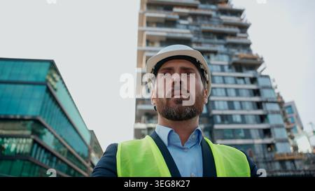 Caucasian man adult contractor in helmet reflective vest looking around city middle-aged male wear hardhat architect pensive thinking urban building Stock Photo