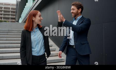 Caucasian business male female walking in city discuss coworkers give high five outdoors two colleagues businessman businesswoman happy man woman Stock Photo