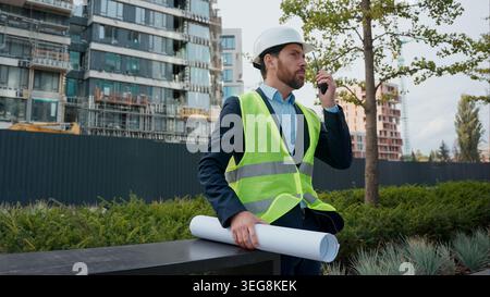 Caucasian man builder engineer in hardhat talking walkie talkie blueprints plan urban city development buildings electricity business engineering male Stock Photo