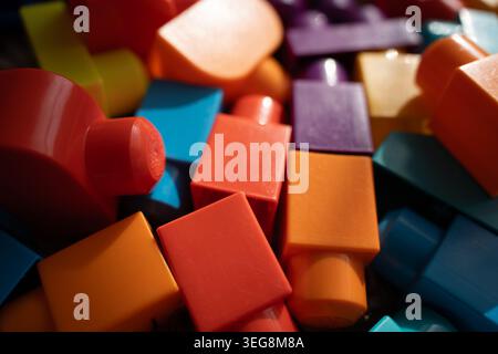 close-up of colorful plastic building blocks piled in warm natural light, shallow depth-of-field emphasizing glossy red, orange, blue and purple recta Stock Photo