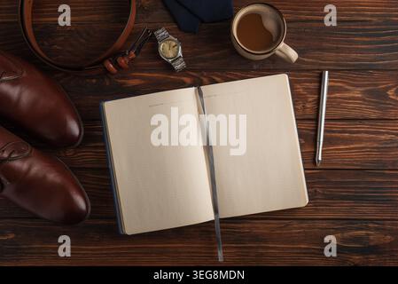 Arranging men's formal accessories—leather shoes, belt, watch, tie, pen, notebook and coffee—on dark rustic wood for a stylish Father's Day gift flat Stock Photo