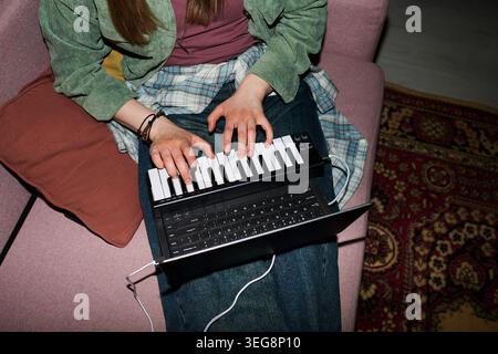 Young Woman Creating Music on Midi Keyboard with Laptop at Home Stock Photo