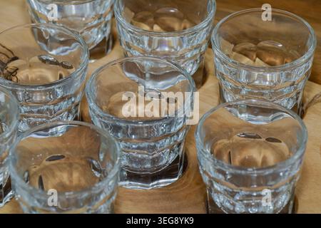 Close-up of empty transparent shot glasses arranged on a wooden tray with reflective surfaces and clean composition. Stock Photo