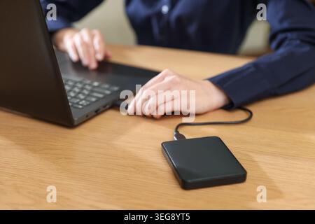 Woman connecting external hard drive to laptop at wooden desk, closeup Stock Photo