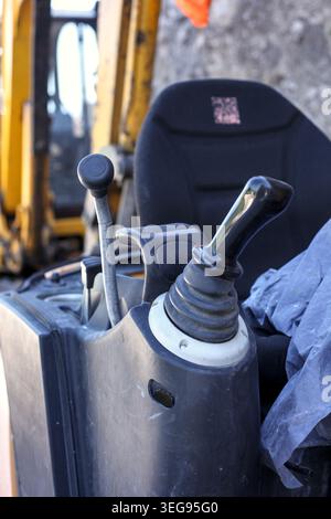 Interior view of a modern excavator operator cabin showing control joysticks, safety levers, and floor pedals. Stock Photo