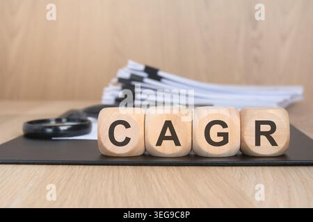 Wooden blocks with the word CAGR on office desk with financial documents and magnifying glass. Concept of compound annual growth rate, financial analy Stock Photo