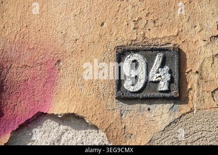 Weathered cast iron address sign with number 94 on textured orange wall with large copy space area. Stock Photo