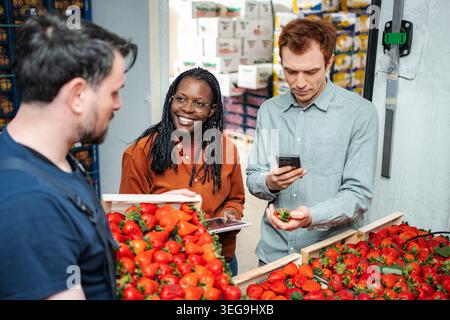 Workers inspecting strawberries using digital devices in distribution warehouse Stock Photo