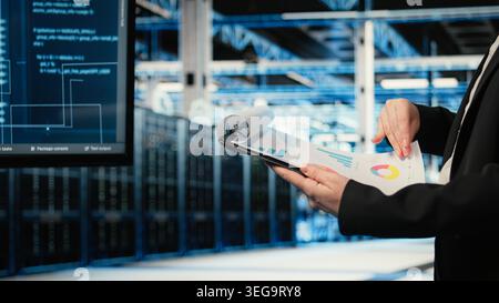 Close up of data center engineer reading clipboard files charts, verifying infrastructure supercomputers status. Server hub expert using audit charts to analyze gear rigs performance Stock Photo