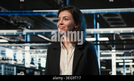 Smiling manager inspecting futuristic data center with blue wireframe mesh overlay. Happy IT professional walking through server room rows visualizing digital twin data streams Stock Photo