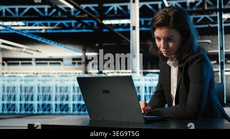 Optimizing server, laptop and software developer in data center doing load balancing. Adjusting system parameters, notebook and woman in server farm at desk improving efficiency Stock Photo