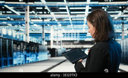 Data center programmer coding on tablet, optimizing equipment rigs using application. Close up of IT professional in server hub running programming script, adjusting system parameters Stock Photo