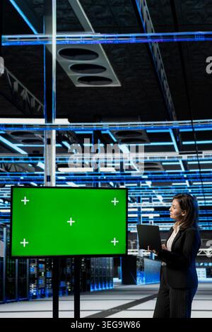 Isolated screen display used by data center female system administrator to configure servers hosting digital services. Woman in server hub uses large mockup monitor to repair infrastructure rackmounts Stock Photo