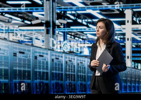 Server farm employee walking through supercomputer rows, looking at computer graphics HUD visualizations. Data center professional analyzing AR infrastructure virtualization mapping Stock Photo