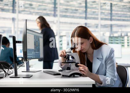 Researcher in microchip factory RD office analyzing microelectronic circuits with laboratory microscope at workstation. Female engineer inspecting PCB parts with optical equipment in research facility Stock Photo