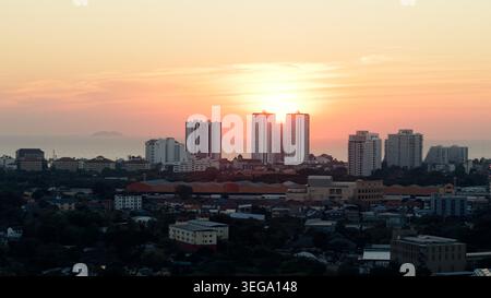 Pattaya city skyline with sun setting behind high rise buildings over ocean Stock Photo