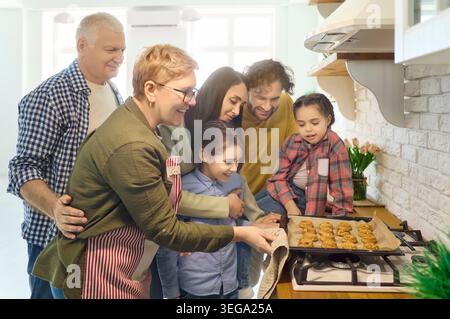 Happy multigenerational family taking cookies from oven in cozy home kitchen Stock Photo