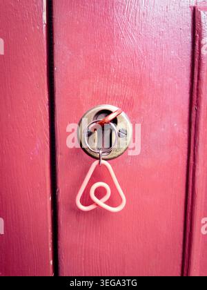 A close-up view of an Airbnb logo keychain hanging from a key inserted into a brass cylinder lock on a weathered pink wooden door. Stock Photo