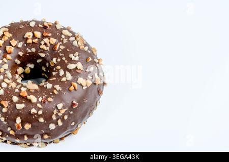 Minimal close-up composition of a chocolate glazed donut topped with chopped nuts on a clean light background with copy space. Modern bakery dessert c Stock Photo