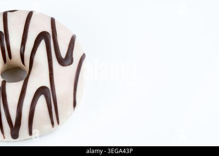 Close-up of a white glazed donut with dark chocolate drizzle isolated on a clean light background with copy space. Minimal bakery dessert concept for Stock Photo