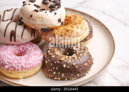 Selection of assorted gourmet donuts with colorful toppings and glazes arranged on a ceramic plate over marble background with copy space. Sweet baker Stock Photo