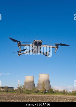 drone hovering mid-air against a clear blue sky, with two industrial cooling towers of a power plant visible in the background. Stock Photo