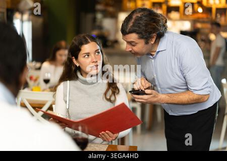 Woman ordering from waiter sitting at table with man Stock Photo
