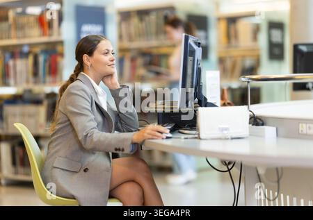 Girl searches for information on the internet using computer in university library Stock Photo