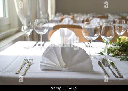 Festive table settings in large room with white napkins, tablecloths, glasses, cutlery and floral decorations for a large holiday dinner, selected foc Stock Photo