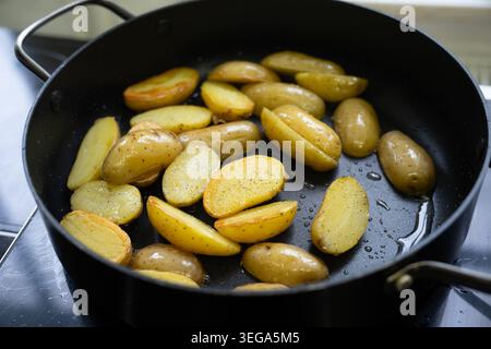 New potatoes with their skins on are cut in half, seasoned, and fried in a black pot on the stove, healthy cooking with fresh, organic ingredients, se Stock Photo