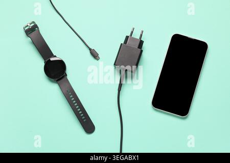 Modern power adapter, USB cable, smart watch and mobile phone with blank screen on turquoise background, top view Stock Photo