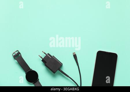 Modern power adapter, USB cable, smart watch and mobile phone with blank screen on turquoise background, top view Stock Photo