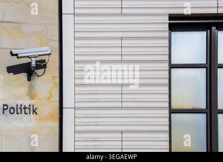 Close-up of a surveillance camera mounted on a building facade beside the word “Politik”, creating a visual concept of security and monitoring. Stock Photo