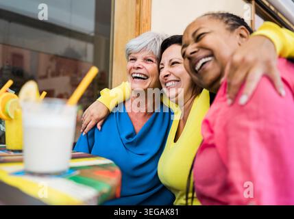 Multiracial senior friends having fun outside bar restaurant while drinking healthy smoothies - Focus on left woman face Stock Photo