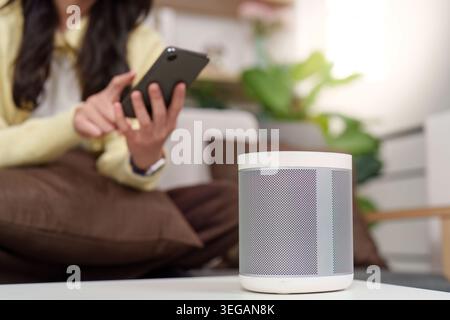 Asian woman using smartphone with smart speaker in modern home Stock Photo