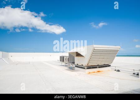 A metal HVAC air conditioning unit and heavy ventilation equipment stand on a flat white industrial roof covered with a waterproof membrane. Stock Photo