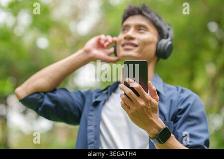 Asian man listening to music with headphones and smartphone in outdoor park Stock Photo
