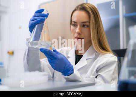Laboratory technician analyzing a clear liquid contained in a conical flask during a scientific experiment. Stock Photo