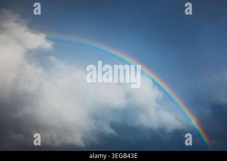 Vibrant Rainbow Arch Against a Deep Blue Sky and White Clouds Stock Photo