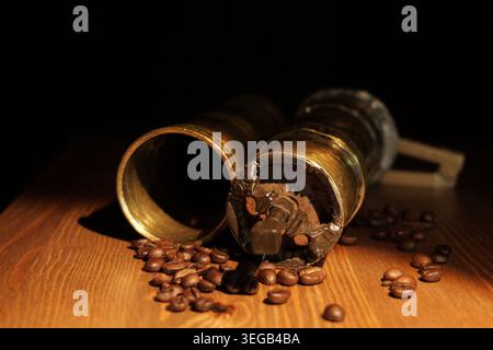 Antique brass manual coffee grinder lying next to scattered aromatic roasted coffee beans on a rustic wooden surface, creating a warm, cozy atmosphere Stock Photo