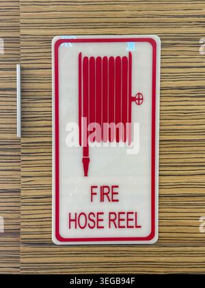 Johor, Malaysia, May 13, 2026: Red and white fire hose reel sign mounted on wood‑patterned wall, indicating emergency firefighting equipment. Stock Photo